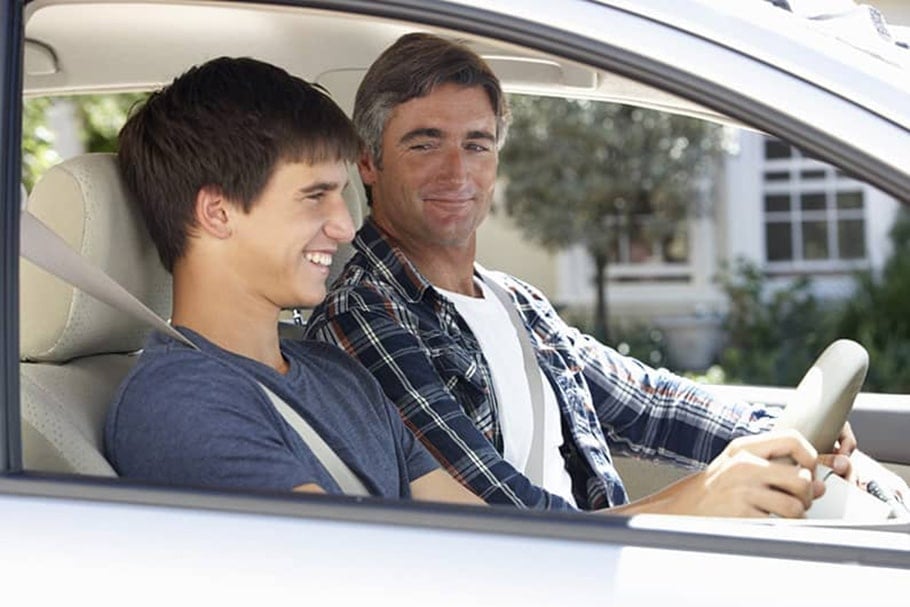 Father smiling while teaching his teenage son to drive