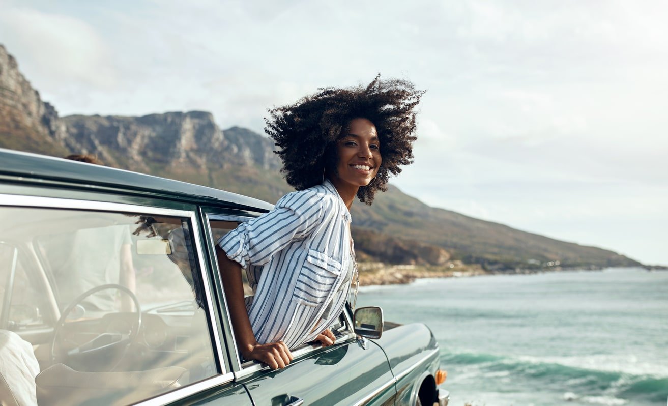 A woman smiling near the ocean on her road trip.