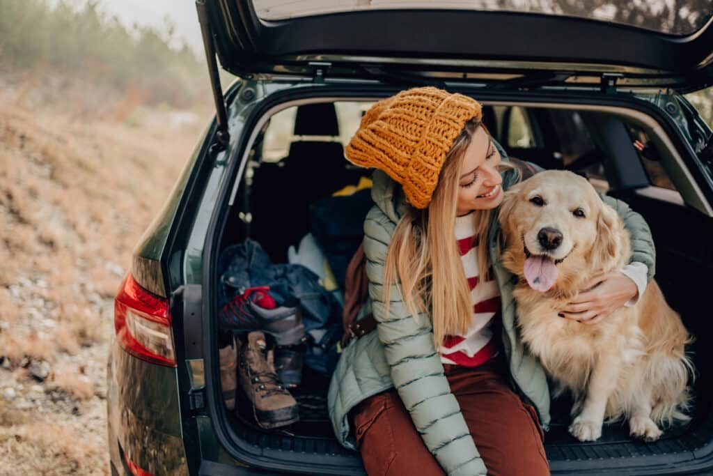 A woman petting her dog in the back of a car as they take a break from their road trip.