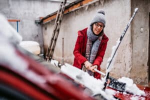 Woman removing snow and ice buildup from her car - winterizing a car.