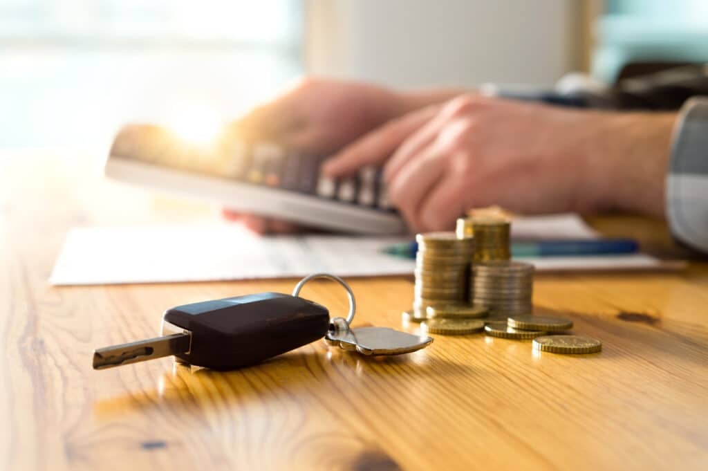 Man calculating his car loan balance - car keys and coins on a table - upside-down car loan concept.