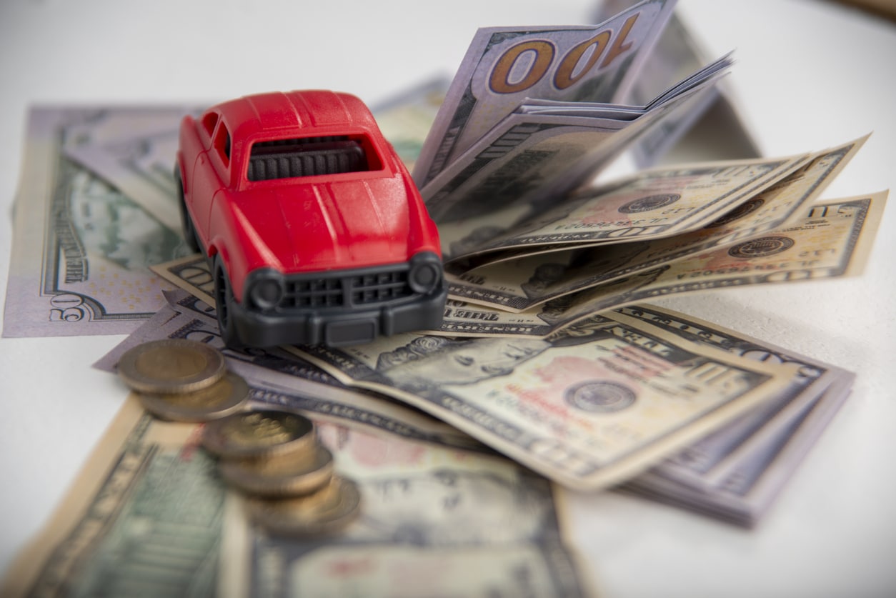 Miniature car model surrounded by dollar bills and coins - paying for auto insurance.
