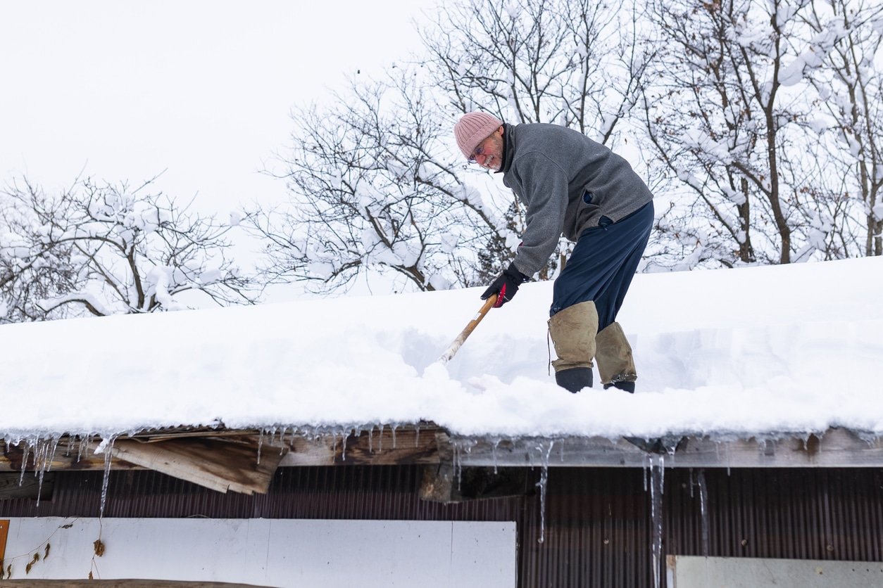 Man shoveling snow from his home's roof - preventing the formation of ice dams.