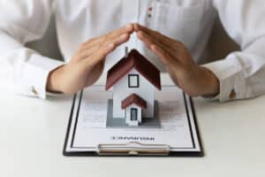 A concept of homeowners insurance - Man covering a miniature house model with his hands.
