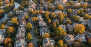 Aerial view of a historic residential neighborhood in Arlington, Massachusetts, showcasing tree-lined streets, large homes with gabled roofs, and a river winding through the autumnal landscape.